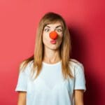 Person wearing red clown nose against a red background.