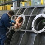 Factory worker using grinder on large metal component.