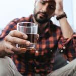 close up shot of depressed young man with glass of whiskey