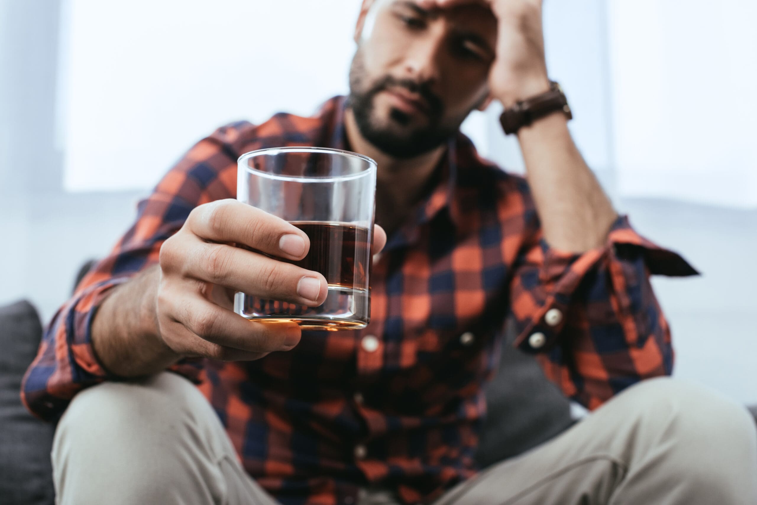 close up shot of depressed young man with glass of whiskey